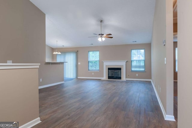 unfurnished living room with dark wood-style floors, ceiling fan, a glass covered fireplace, and baseboards
