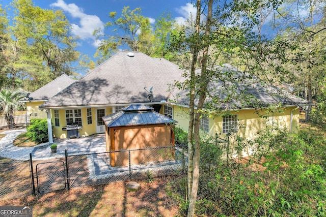 rear view of property with a gate, a gazebo, stucco siding, metal roof, and a fenced front yard