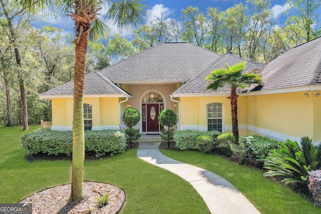 view of front of house with a shingled roof, stucco siding, and a front lawn