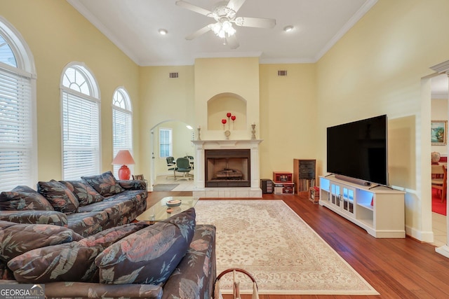 living area with visible vents, ornamental molding, wood finished floors, a towering ceiling, and a ceiling fan