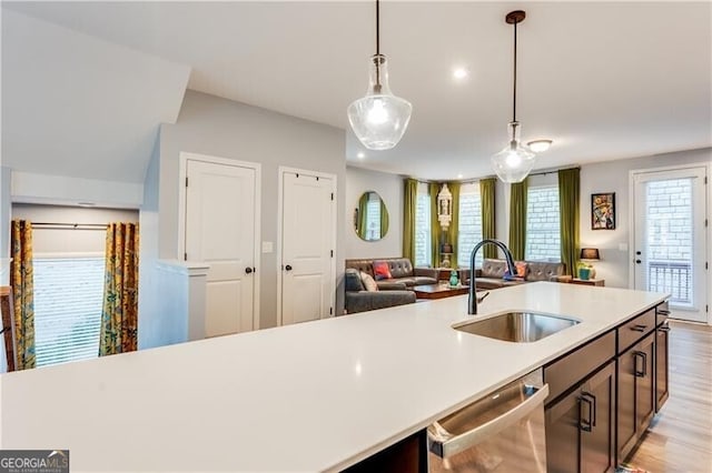 kitchen featuring light countertops, dishwasher, a sink, open floor plan, and pendant lighting