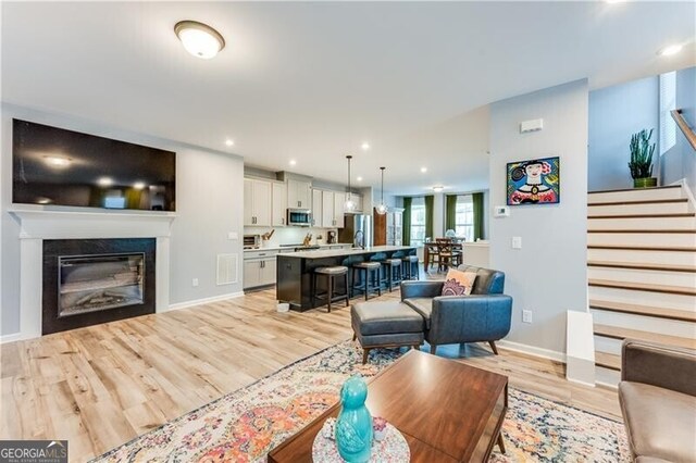 living room featuring stairway, light wood finished floors, a glass covered fireplace, baseboards, and recessed lighting