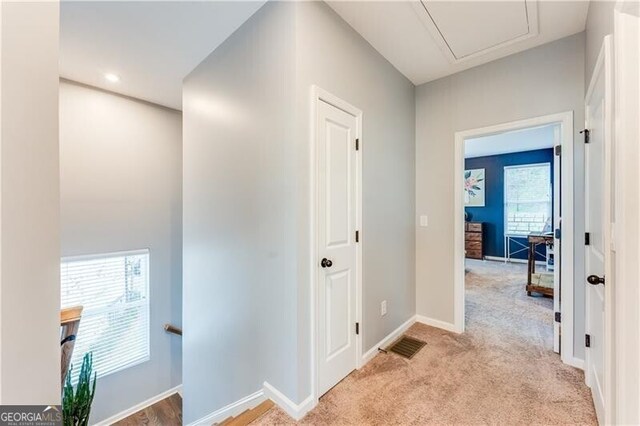 corridor with baseboards, light colored carpet, and visible vents