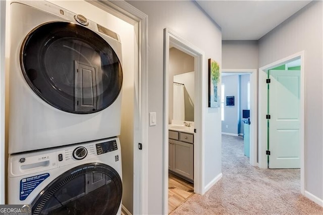 clothes washing area featuring light carpet, baseboards, stacked washer / dryer, and laundry area