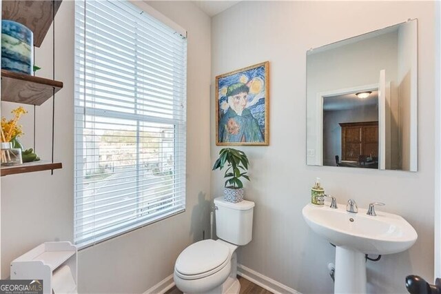half bathroom with toilet, plenty of natural light, and baseboards