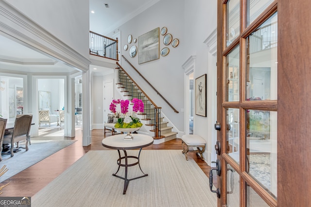 foyer entrance with a high ceiling, crown molding, wood finished floors, and stairway