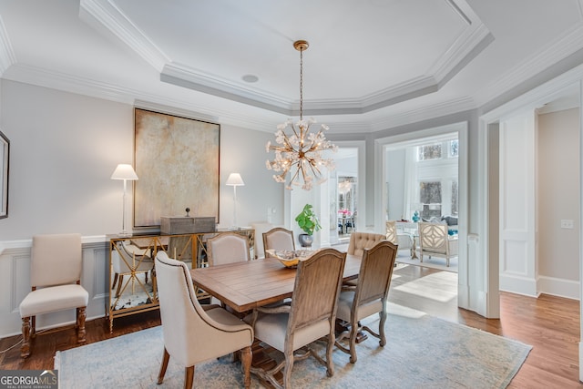 dining space featuring an inviting chandelier, a raised ceiling, crown molding, and wood finished floors