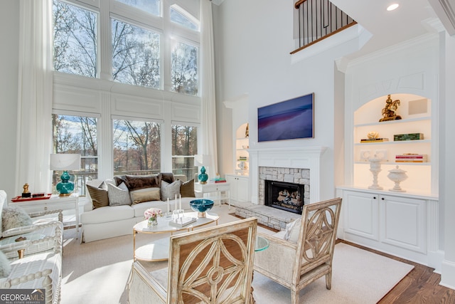 living room featuring wood finished floors, plenty of natural light, a stone fireplace, and built in shelves
