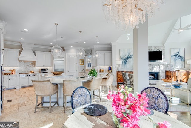 dining area with a fireplace, stone tile flooring, ceiling fan with notable chandelier, ornamental molding, and recessed lighting