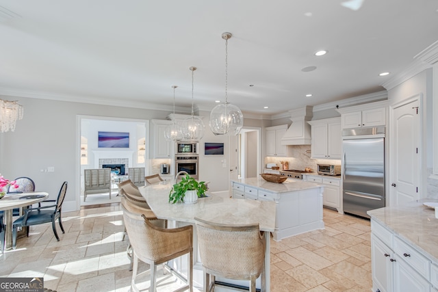 kitchen with built in appliances, a fireplace, premium range hood, a center island, and stone tile flooring