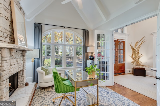 office space featuring a stone fireplace, beamed ceiling, high vaulted ceiling, and wood finished floors