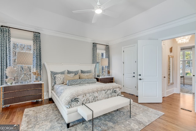 bedroom featuring a tray ceiling, ceiling fan with notable chandelier, crown molding, and wood finished floors