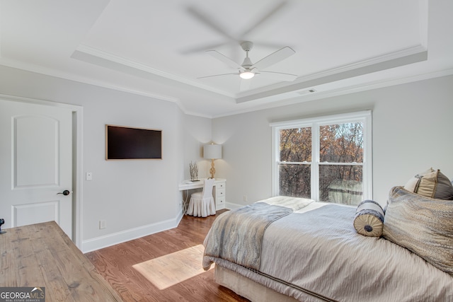 bedroom featuring a tray ceiling, baseboards, visible vents, and wood finished floors