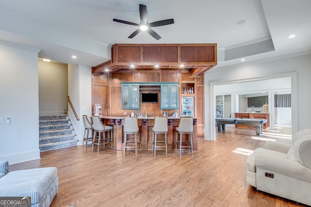 interior space featuring ceiling fan, crown molding, light wood-style floors, and a kitchen breakfast bar