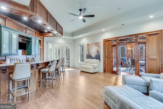 living area featuring bar area, crown molding, light wood-type flooring, ceiling fan, and visible vents