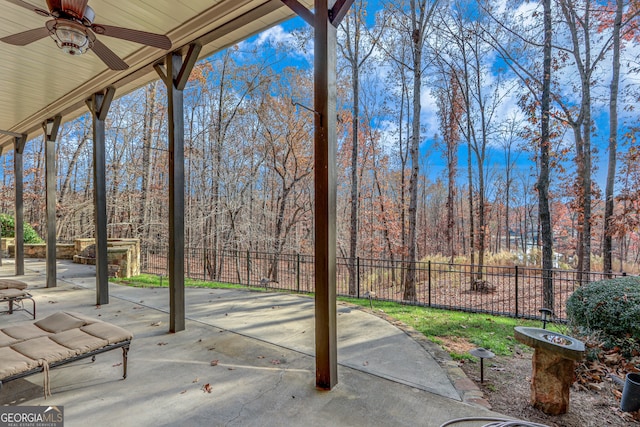 view of patio featuring fence, a forest view, and a ceiling fan