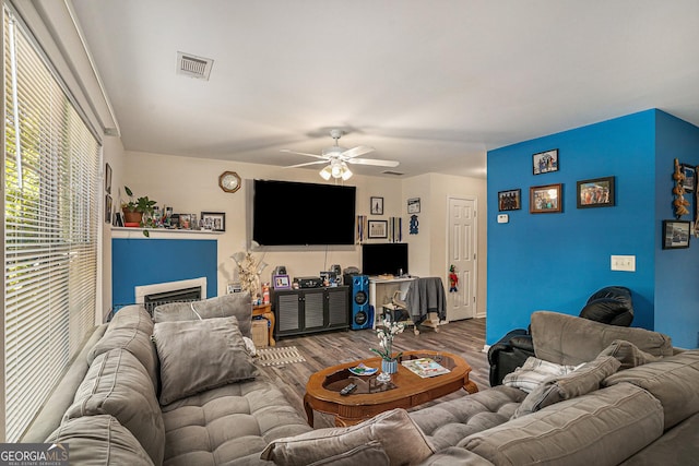 living room with ceiling fan, visible vents, wood finished floors, and a fireplace