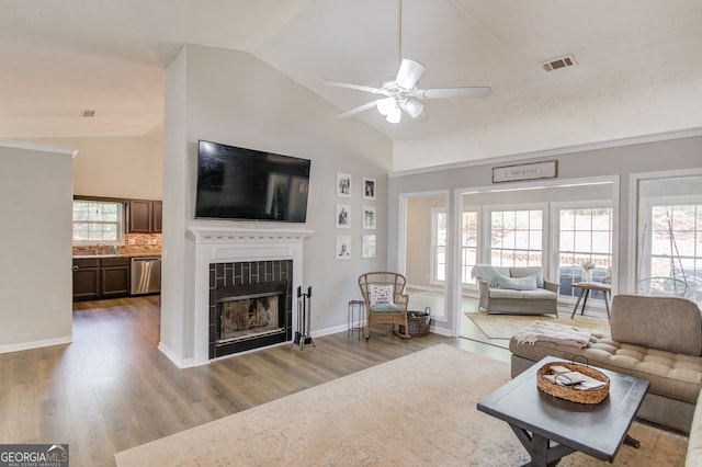 living area featuring a tiled fireplace, visible vents, lofted ceiling, a ceiling fan, and wood finished floors