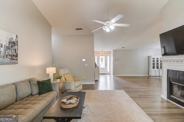 living room with wood finished floors, visible vents, baseboards, a tiled fireplace, and ceiling fan