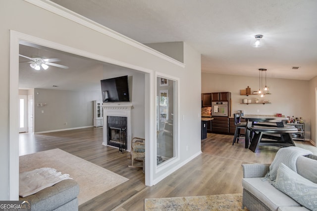 living room with visible vents, light wood-style floors, baseboards, a fireplace, and ceiling fan with notable chandelier
