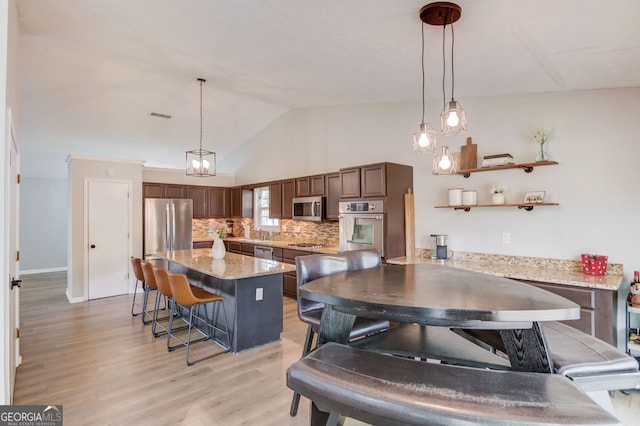 kitchen with stainless steel appliances, a kitchen breakfast bar, tasteful backsplash, light wood-type flooring, and decorative light fixtures