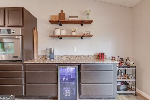 bar featuring light wood finished floors, wine cooler, oven, baseboards, and a bar