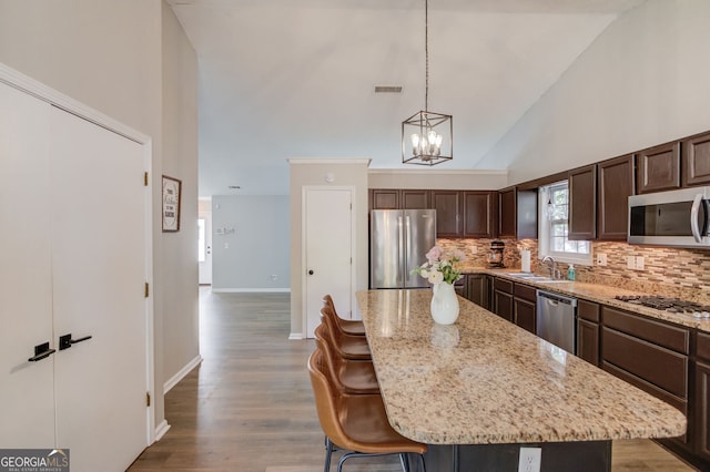 kitchen with backsplash, dark brown cabinets, a sink, a center island, and appliances with stainless steel finishes