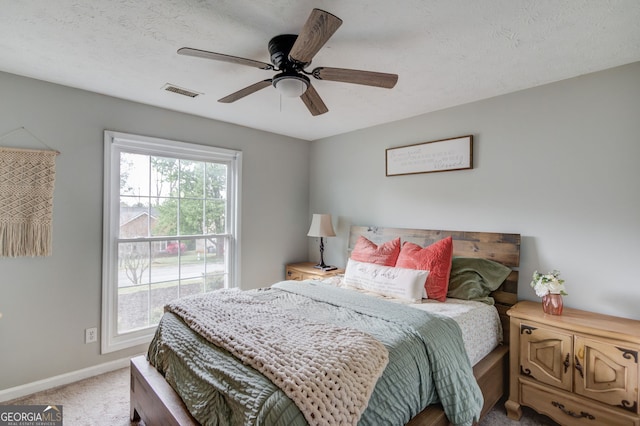 carpeted bedroom featuring a textured ceiling, visible vents, a ceiling fan, and baseboards