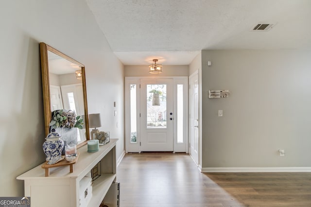 foyer entrance with wood finished floors, a textured ceiling, an inviting chandelier, baseboards, and visible vents