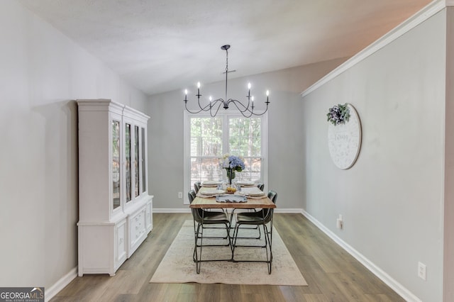dining space featuring vaulted ceiling, wood finished floors, a chandelier, and baseboards