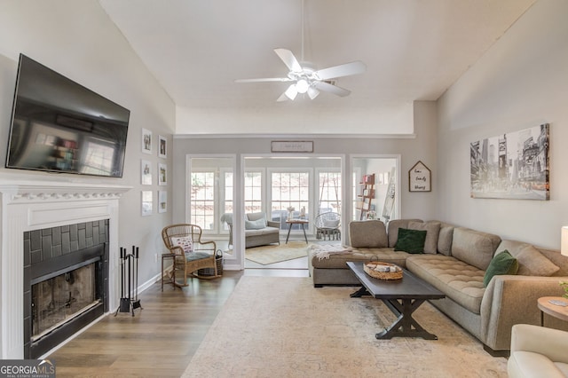 living room featuring a tile fireplace, ceiling fan, baseboards, and wood finished floors