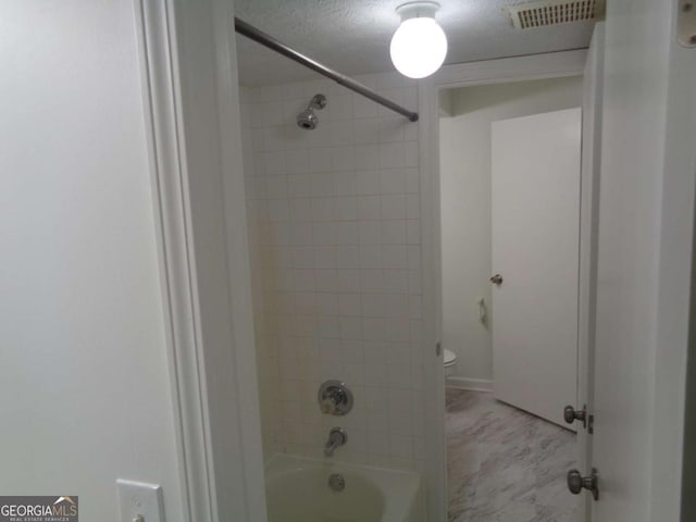 bathroom with a textured ceiling, visible vents, toilet, and shower / bath combination