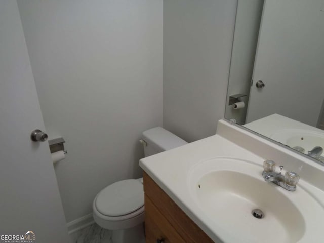 half bath with baseboards, toilet, and vanity