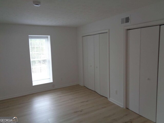 unfurnished bedroom featuring baseboards, multiple closets, visible vents, and light wood-type flooring
