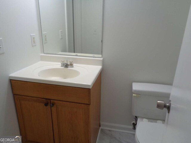 half bath with baseboards, marble finish floor, toilet, and vanity