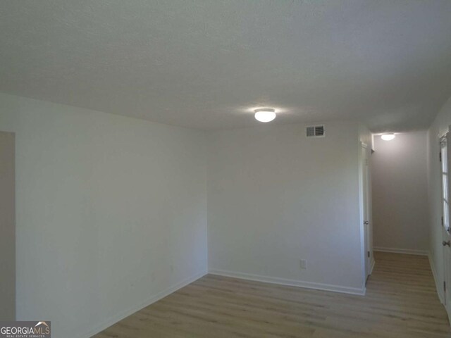 unfurnished room with light wood finished floors, baseboards, visible vents, and a textured ceiling