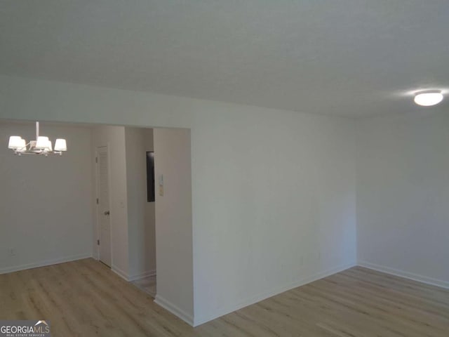 spare room with a notable chandelier, baseboards, and light wood finished floors