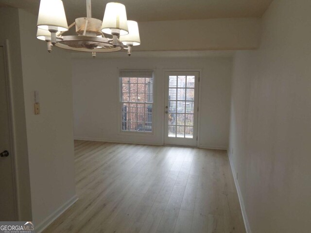 spare room with baseboards, light wood-type flooring, and a chandelier