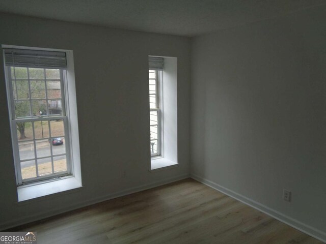 spare room featuring plenty of natural light, baseboards, and wood finished floors