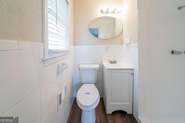 full bathroom featuring wood finished floors, a tile shower, toilet, visible vents, and wainscoting