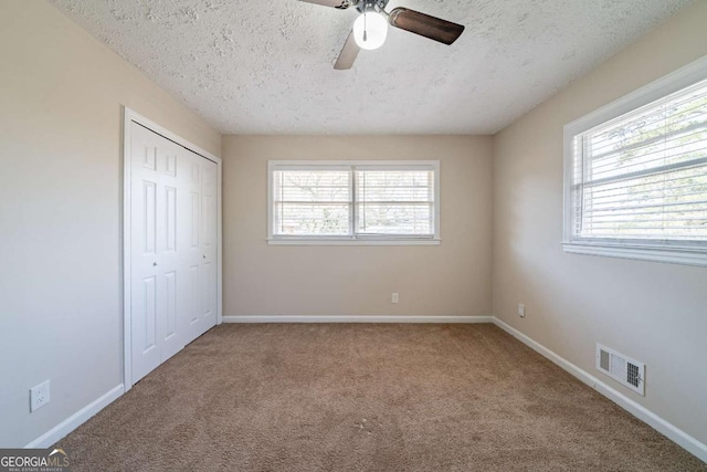 unfurnished bedroom featuring a closet, a textured ceiling, visible vents, baseboards, and carpet floors