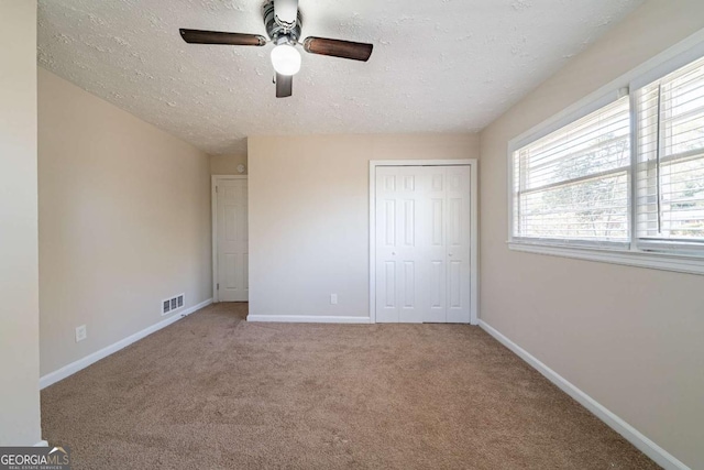 unfurnished bedroom featuring baseboards, a textured ceiling, carpet floors, visible vents, and a closet