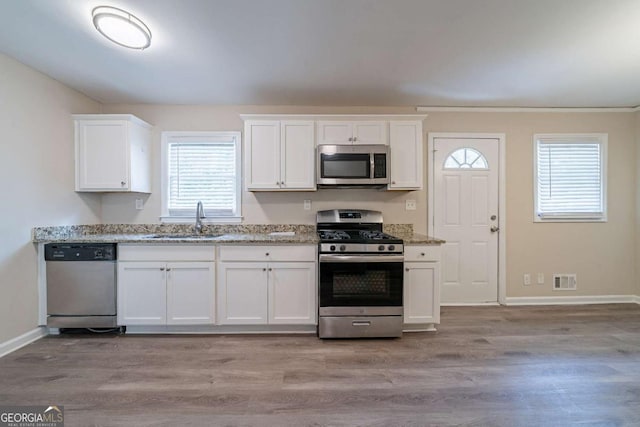 kitchen featuring light stone counters, a sink, white cabinetry, light wood-style flooring, and stainless steel appliances