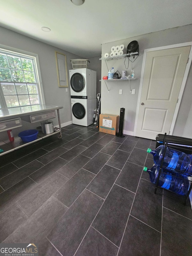 washroom with baseboards, laundry area, stacked washer / dryer, and dark tile patterned flooring