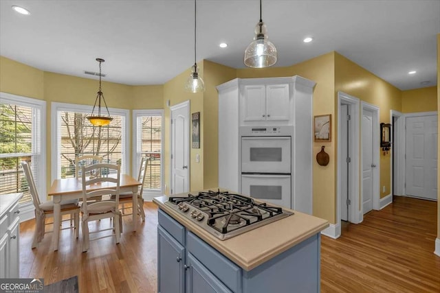 kitchen featuring stainless steel gas cooktop, double oven, white cabinetry, wood finished floors, and visible vents