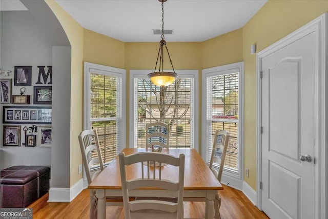 dining area with light wood finished floors, baseboards, visible vents, and arched walkways