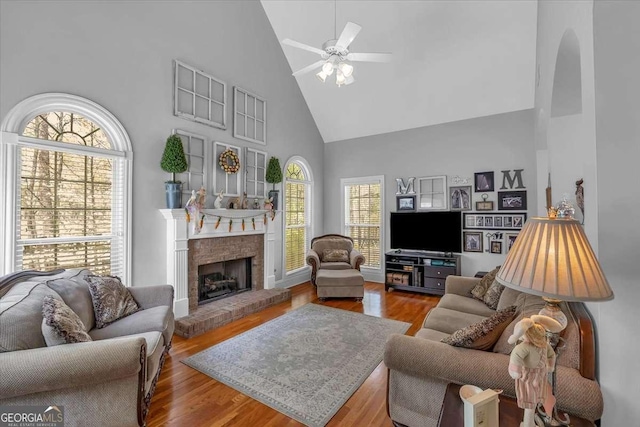 living area with a brick fireplace, high vaulted ceiling, wood finished floors, and a ceiling fan