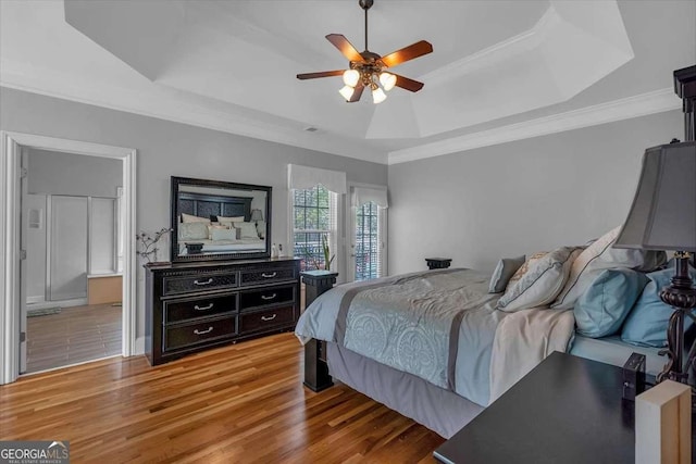 bedroom with a raised ceiling, light wood-type flooring, ensuite bathroom, ceiling fan, and ornamental molding