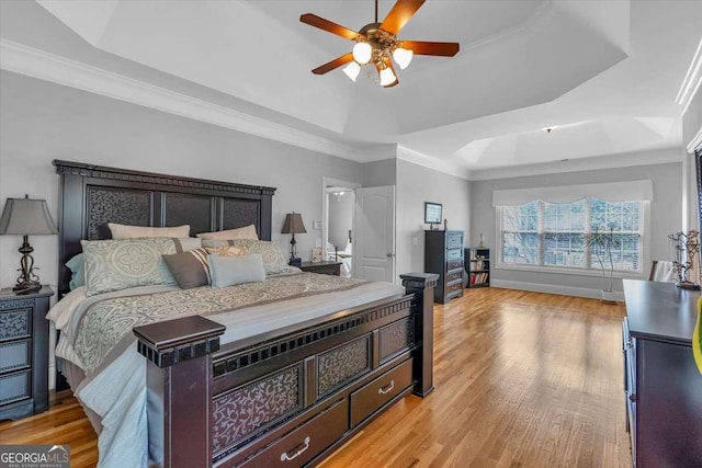 bedroom with baseboards, ornamental molding, light wood-style floors, and a raised ceiling