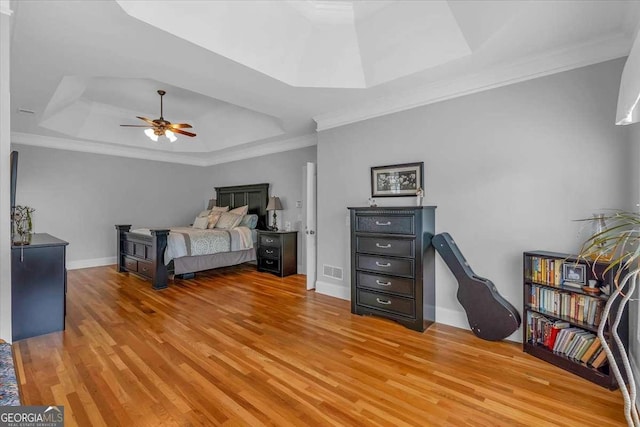 bedroom featuring a raised ceiling, crown molding, light wood-style flooring, and visible vents